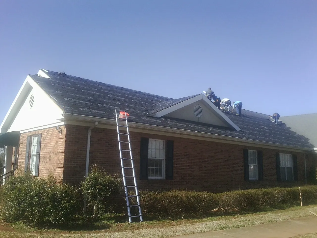 Crew tearing shingles off a brick ranch roof with a ladder set — Emergency Roof Repair work by our crew in Park Rapids