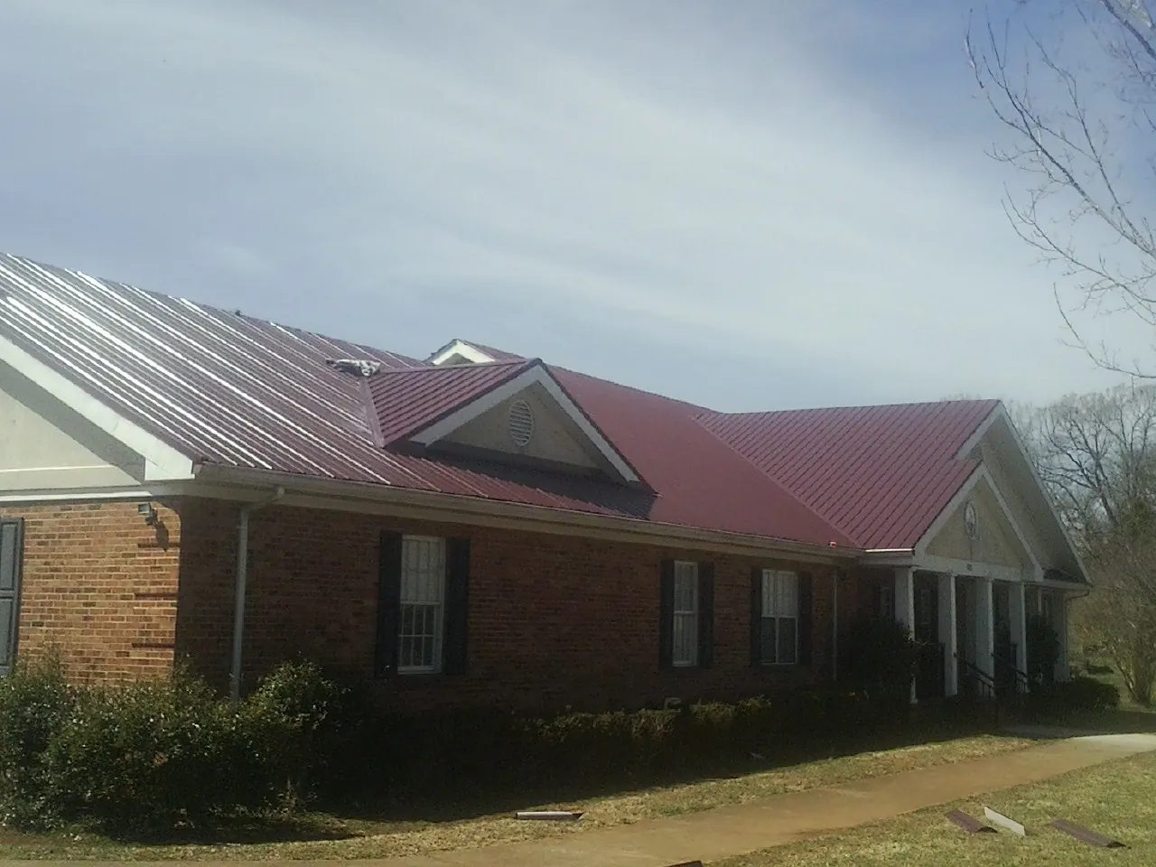 Red metal roof with gabled entries on a long brick building, from a Hail Damage Roof Repair job in Park Rapids