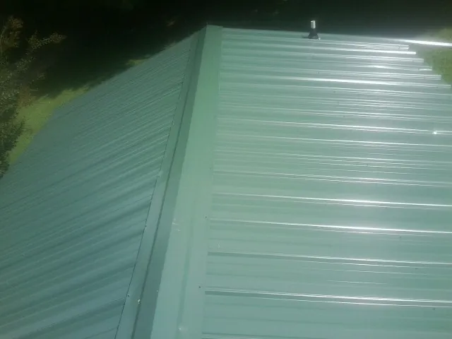 New green metal panels meeting at the ridge of a roof — Flat Roof Repair work by our crew in Park Rapids