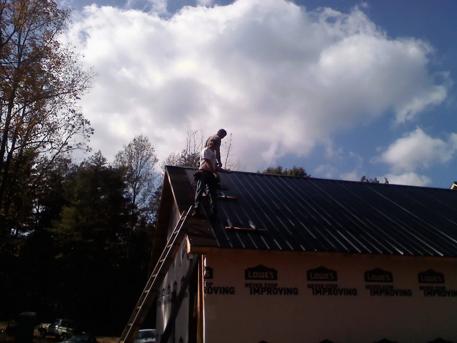 Roofer fastening dark metal panels high against a cloudy sky, from a Roof Inspection job in Park Rapids