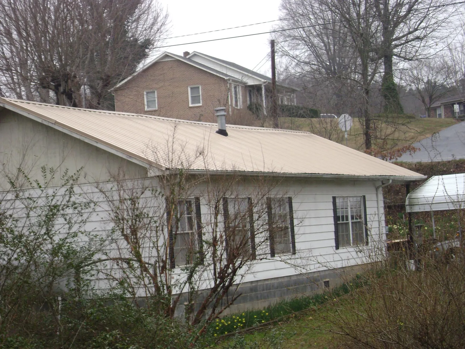 Tan metal roof on a white sided house set into a hillside — Commercial Roofing by Roofing Brothers in Park Rapids