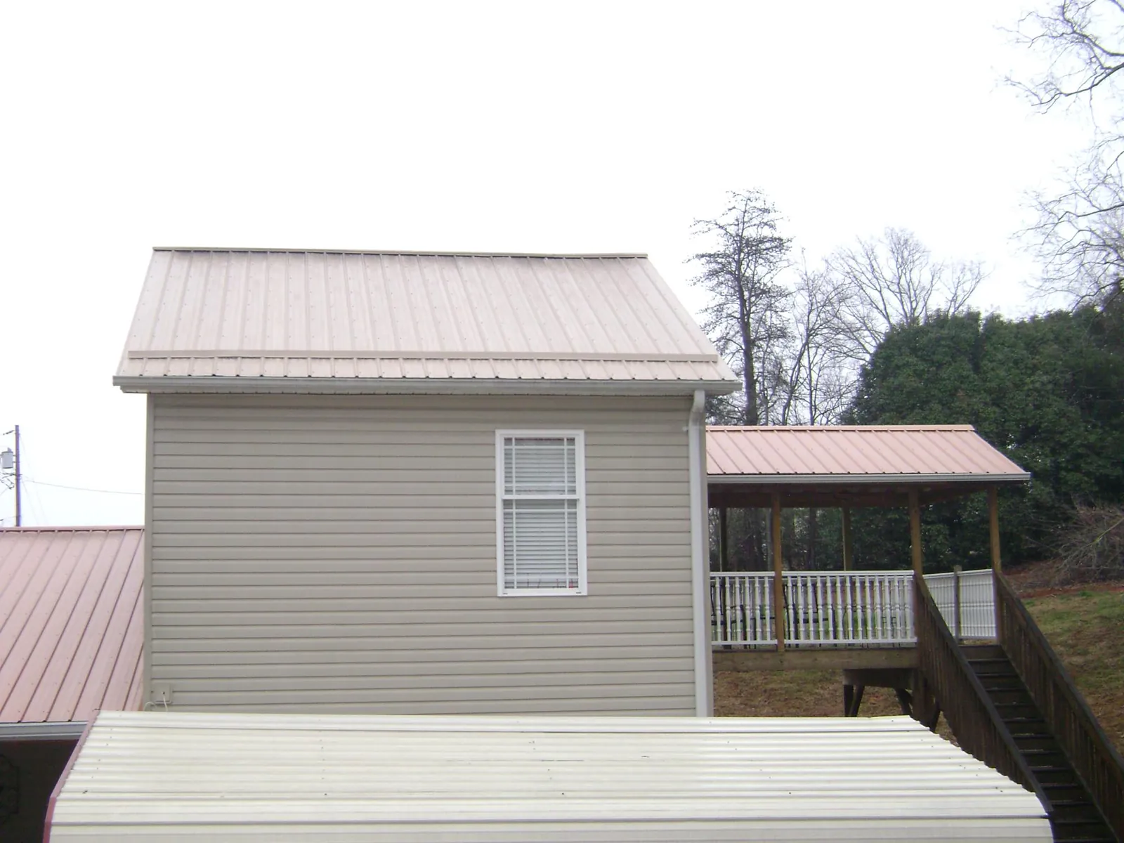 Tan metal roofs on a two story addition and attached porch, from a Roof Replacement job in Park Rapids